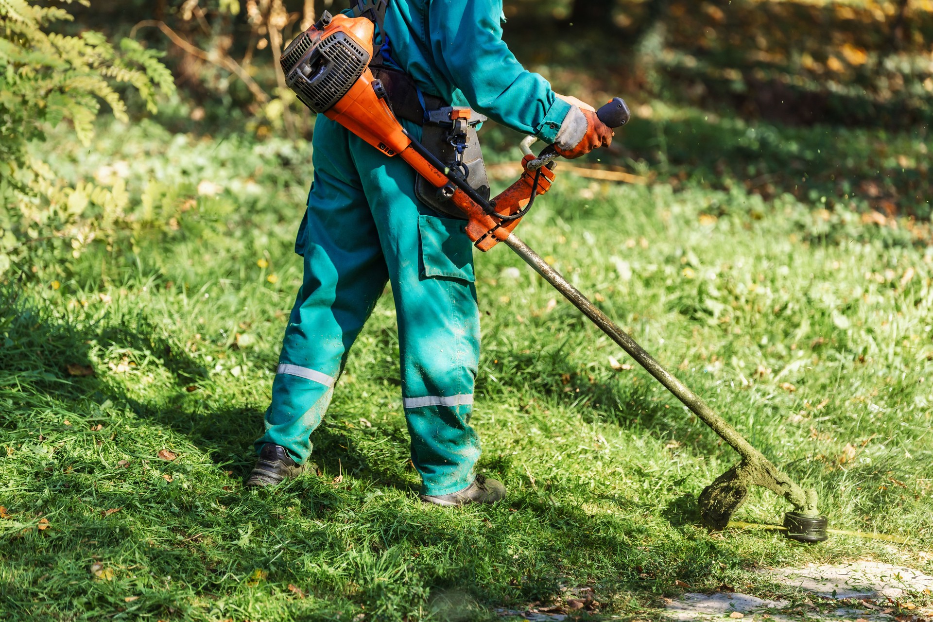 Worker using grass trimmer for landscaping in a green park during sunny afternoon